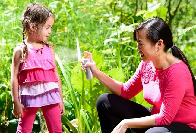 A mother sprays her daughter with sunscreen to prevent sunburn